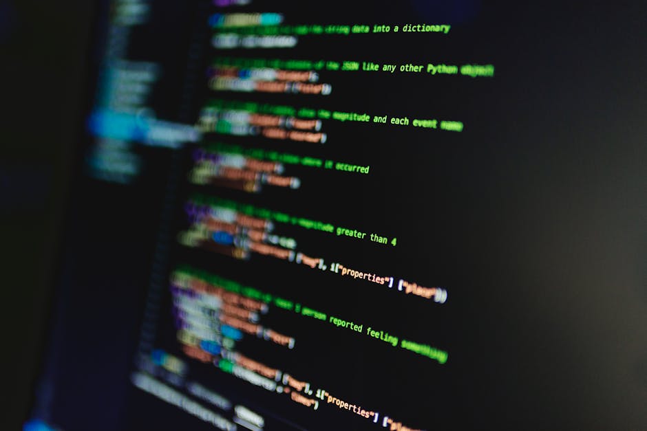A close-up view of a computer screen displaying colorful lines of programming code with green, blue, orange, and purple text on a black background. The focus is on the screen's content, highlighting t